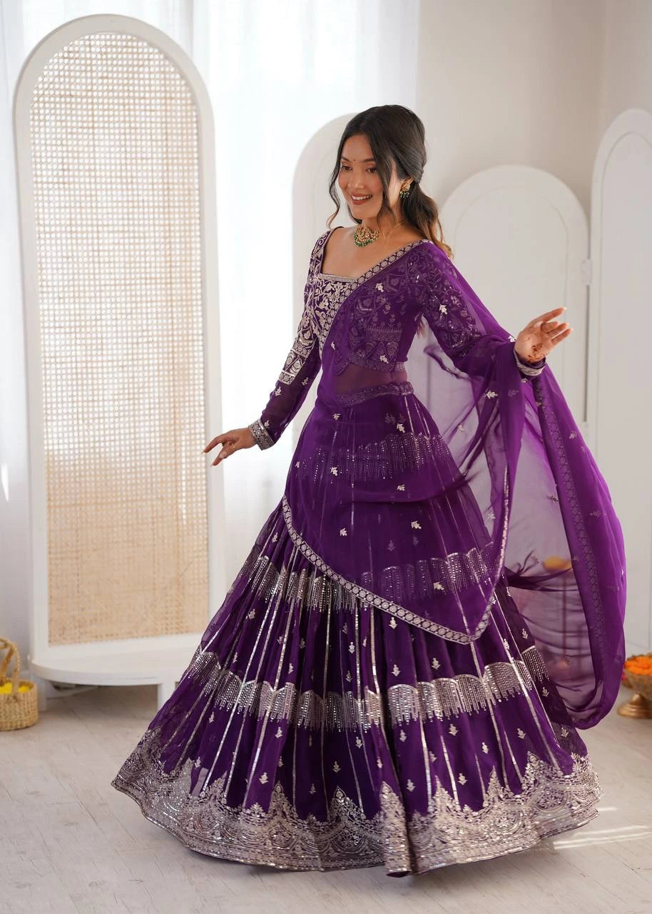 Woman in a purple traditional outfit with silver details, standing against a neutral background.